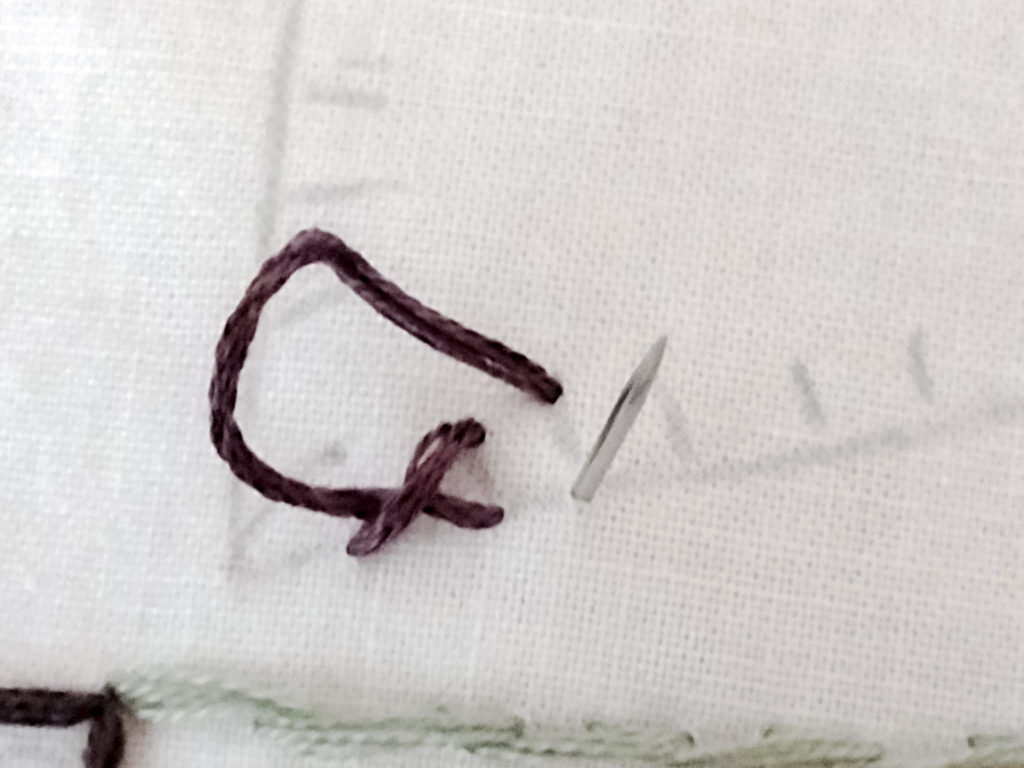 embroidery needle poking through from underneath an embroidery sampler sewing a blanket stitch