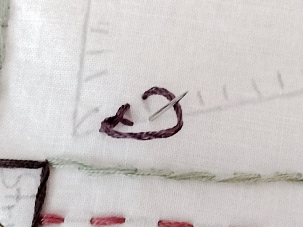 Floss circling an embroidery needle in preparation for making the second blanket stitch