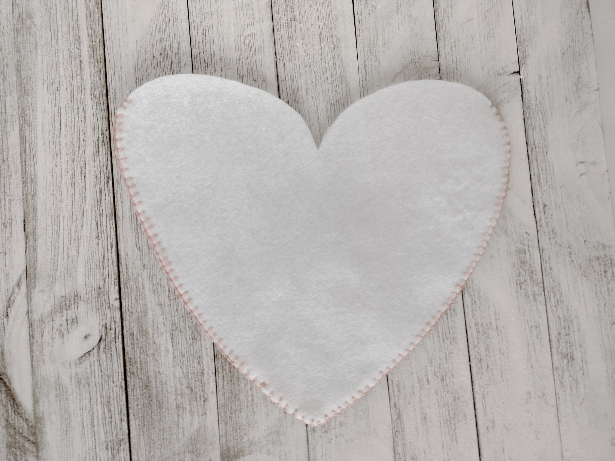 Photo of white felt heart with pink blanket stitch most of the way around
