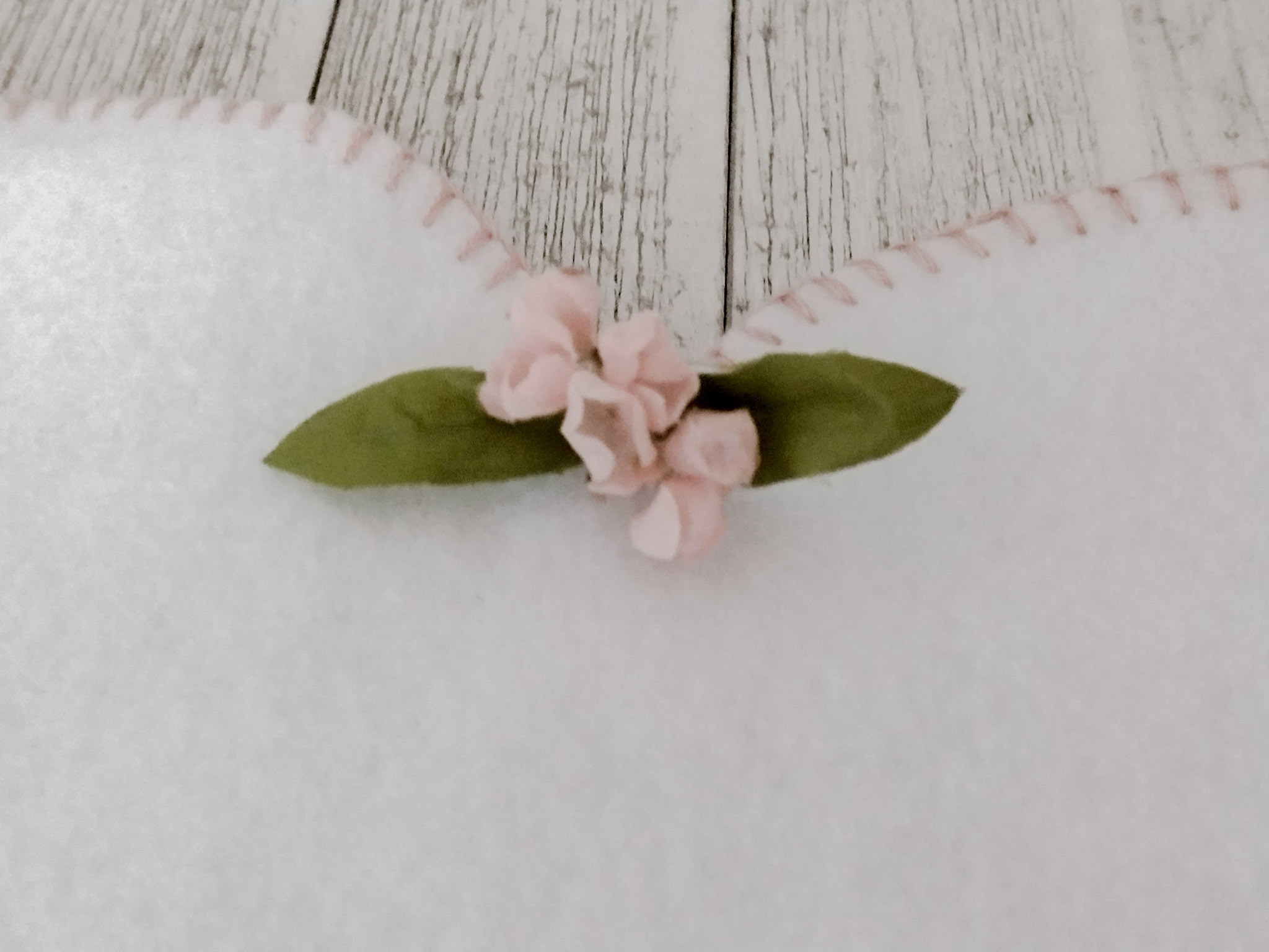 close up of fake pink flowers and two green  sleeves on white felt with pink blanket stitch on the edges