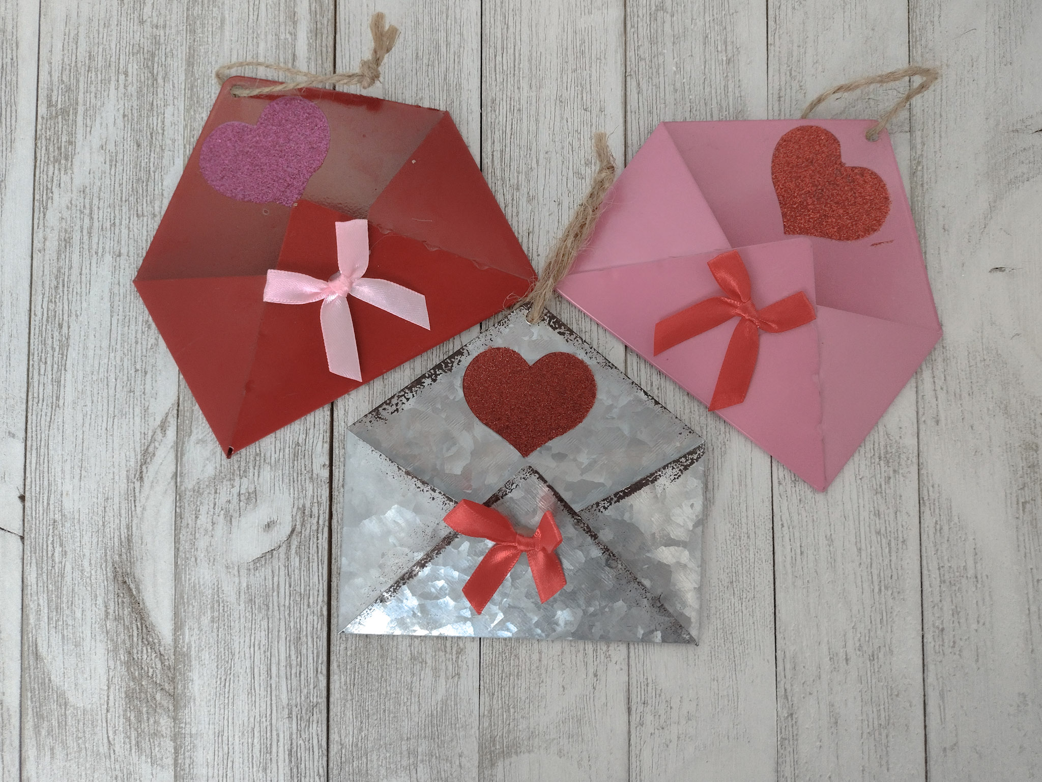 Three metal envelopes in clors of pink, red, and silver