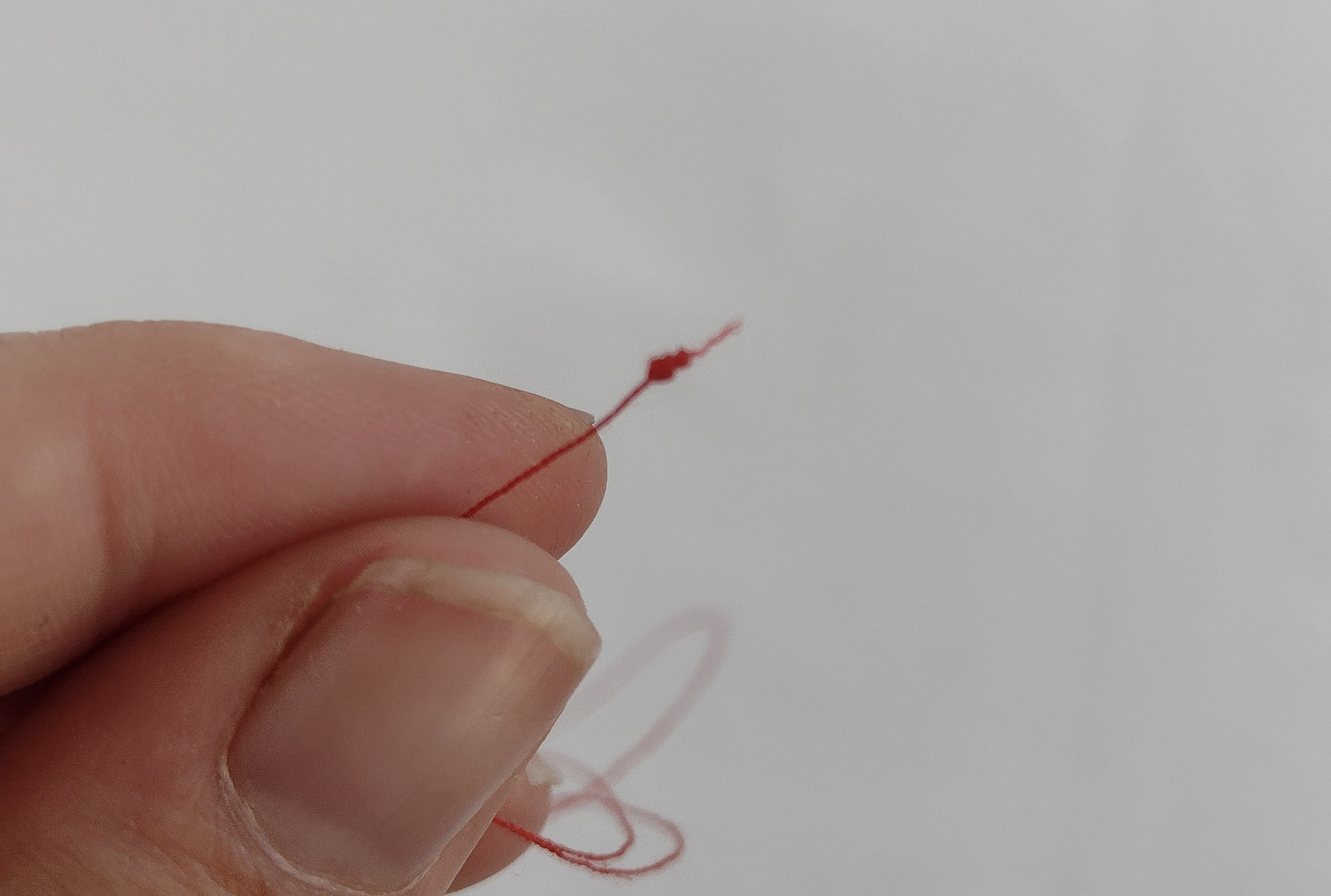 wrapping red thread around a needle to make a knot
